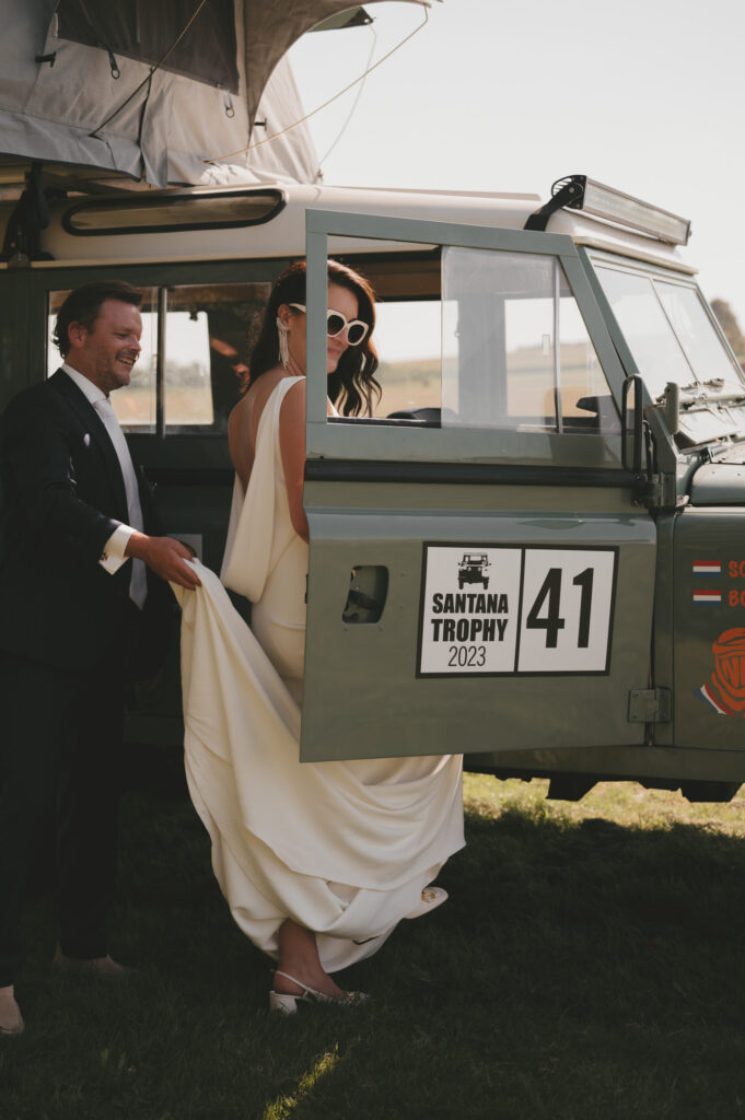 Stijlvolle bruid in een witte trouwjurk stapt in een vintage Land Rover tijdens een luxe destination wedding. Bruidsfotografie door TwentyTwelve Photography